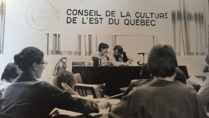 Un podium avec des gens qui parlent, en noir et blanc.