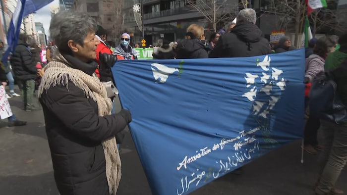 Elahé Chekrai, de l’Association des femmes iraniennes de Montréal, porte un drapeau « Femme, vie et liberté ».