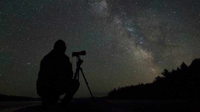 Un ciel étoilé avec une personne qui l'observe à l'aide d'un téléscope.