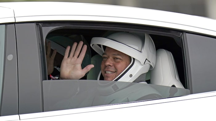 L'astronaute salue de la main, assis dans une voiture avec sa combinaison spatiale.