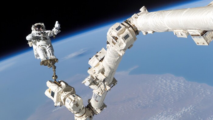 Une photo de l'astronaute américain Stephen K. Robinson perché au bout du Canadarm2 pour effectuer des travaux sur la Station spatiale internationale. 