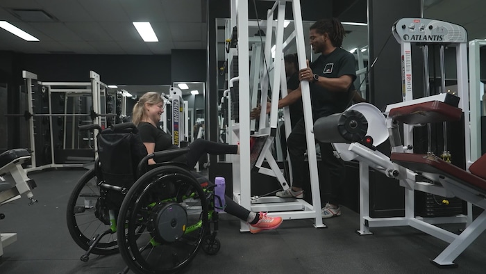 Une femme handicapée sur une machine de musculation aidée par son entraîneur. 
