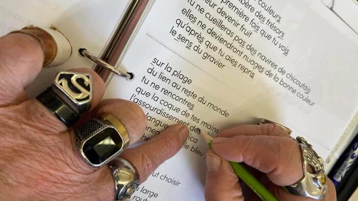 Une main avec un crayon souligne les s dans un poème.