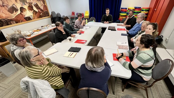 Un groupe de personnes assis à une table discutent, du matériel d'écriture devant eux.