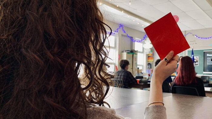 Une adolescente de dos tient un carton dans sa main droite.