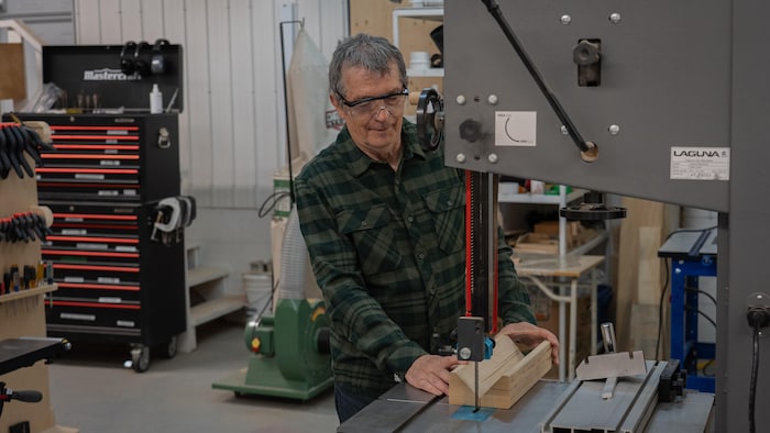 Un homme coupe un bout de bois sur une machine dans un atelier de menuiserie.
