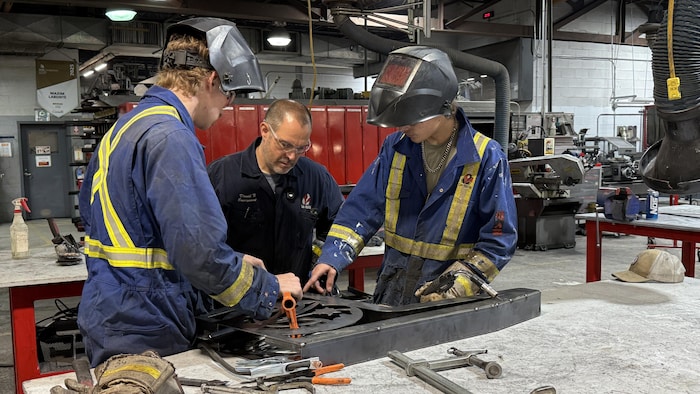Des élèves consultent l'enseignant en métallurgie David Fortin, pour une pièce qu'ils sont en train d'assembler dans l'atelier de soudage.
