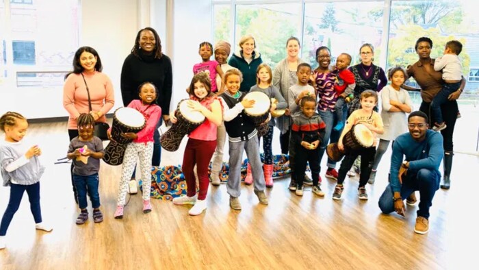 Un groupe de personnes de diverses communautés participent à un atelier de l'organisme. Certains enfants jouent du tambour.
