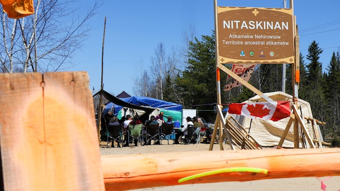 Un panneau avec l'inscription Nitaskinan, Territoire ancestral atikamekw, et des personnes en arrière réunies.