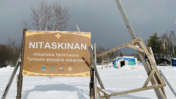 Un panneau avec l'inscription Nitaskinan territoire ancestral atikamekw planté dans la neige.