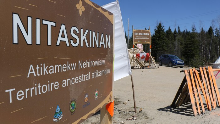 Un panneau avec l'inscription Nitaskinan, territoire ancestral atikamekw et une barrière en plein bois. 