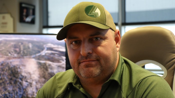 Un homme de face avec une casquette et un polo vert.