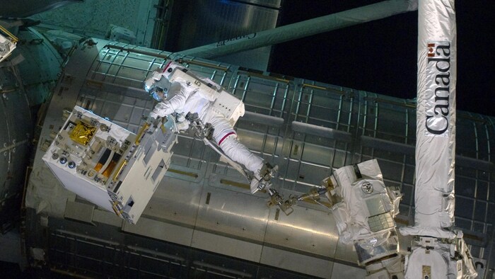 Un astronauta flota en el espacio e intenta reparar un aparato. 