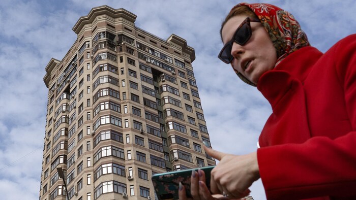 Une femme au pied d'un immeuble endommagé.