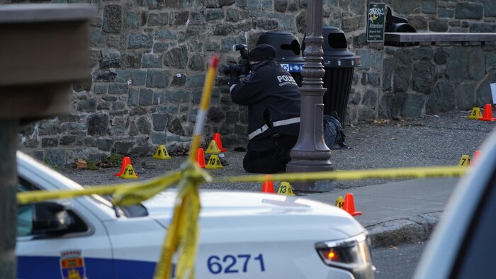 Un policier à genoux prend une photo d'indice dans une rue de Québec.