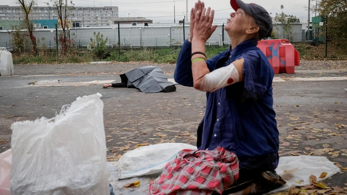 Un vendeur ambulant blessé réagit alors que le corps d’un autre vendeur ambulant gît au sol à côté de ses marchandises sur le site d’un marché aux puces touché par une frappe militaire russe.