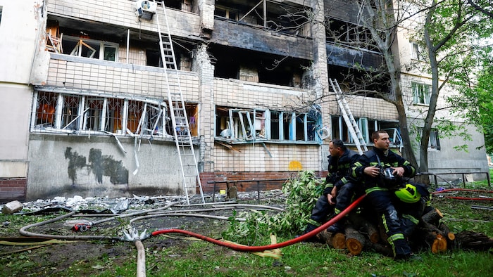 Des pompiers se reposent devant un bâtiment lourdement endommagé par des attaques de drones.