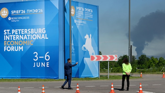 Des personnes devant des banderoles portant le logo du Forum économique international de Saint-Pétersbourg (SPIEF), tandis que de la fumée noire s'élève au loin à Saint-Pétersbourg, le 3 juin 2026.