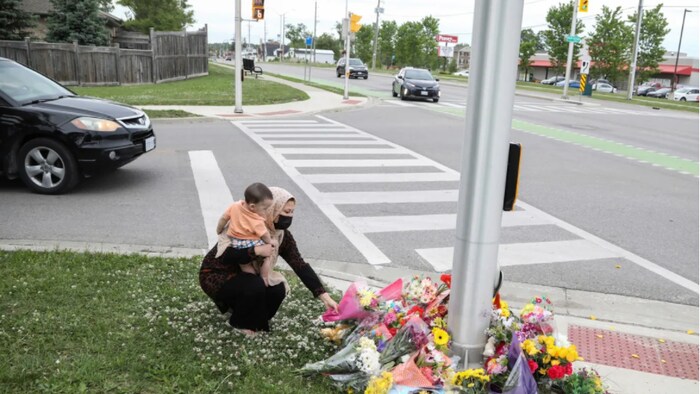Nafisa Azima carries Seena Safdari while laying flowers at the fatal crime scene where a man driving a pickup truck jumped the curb and ran over the Muslim family.