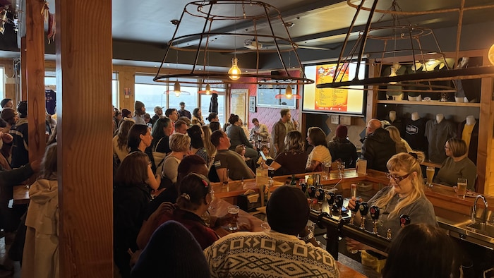 Une centaine de personnes occupe la microbrasserie, où une programmation est projetée.