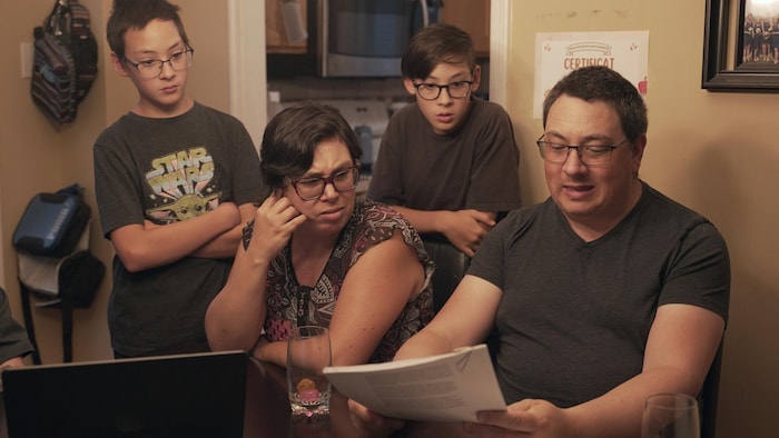 Deux parents et leurs jumeaux réagissent à la lecture d'un document.