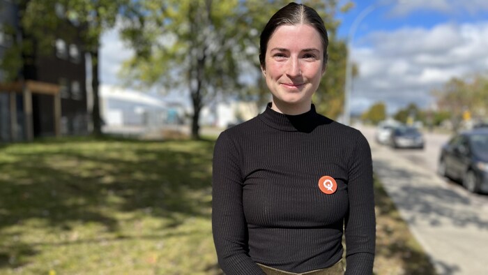 Audrey Givern-Héroux se tient devant les résidences étudiantes. Elle porte un macaron de Québec solidaire sur son chandail.