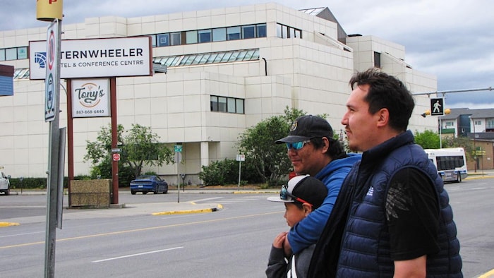 Deux hommes et un garçon attendent l'autobus au bord de la rue à Whitehorse.