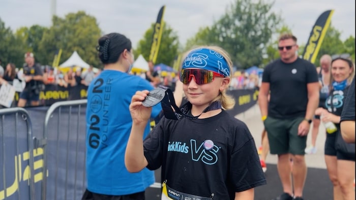 Il tient une médaille de participation dans sa main droite et pose pour une photo.