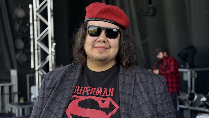 Un homme debout sur une scène regarde la caméra. 