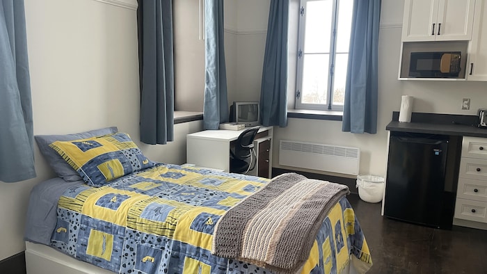 une pièce avec un lit, un bureau et un coin cuisine.