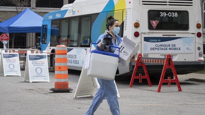 Une professionnelle de la santé marche devant un autobus transformé en clinique de dépistage.