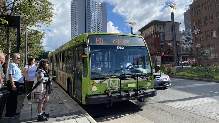 Des usagers s’apprêtent à monter à bord d’un autobus du RTC au centre-ville de Québec en été.