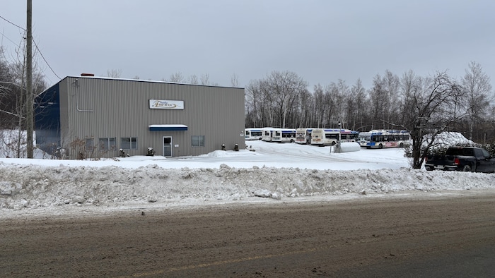 Des autobus de transport en commun sont stationnés près d’un édifice en hiver.