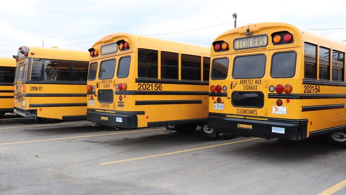 Trois autobus scolaires stationnés.