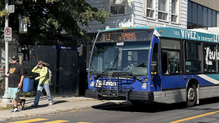 Des piétons marchent près d'un autobus du trajet L2 à un arrêt.