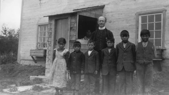 Des enfants autochtones posent avec un prêtre devant un externat dans les Territoires du Nord-Ouest en 1931.
