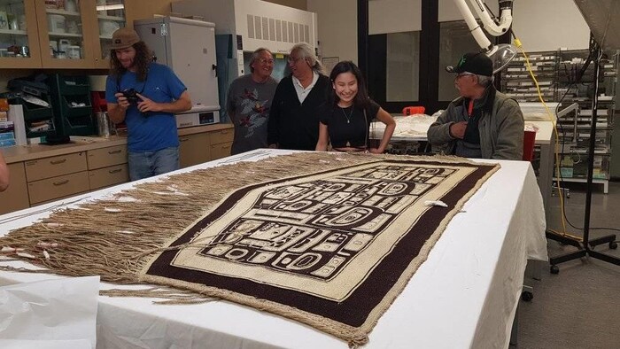 La couverture chilkat sur une table entourée de personnes.