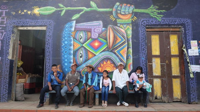 Des Autochtones de Colombie assis sur un banc devant une murale.