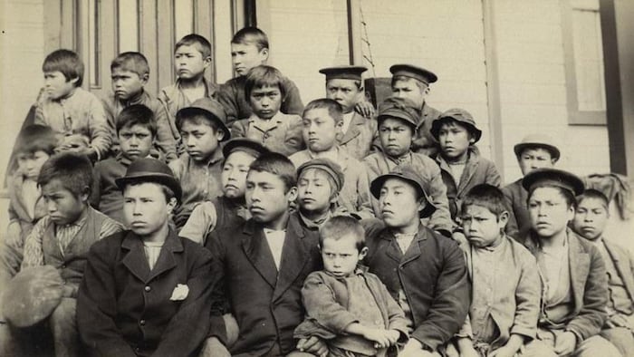 Une vieille photo dépeint un groupe d'une vingtaine de jeunes garçons autochtones devant un bâtiment.