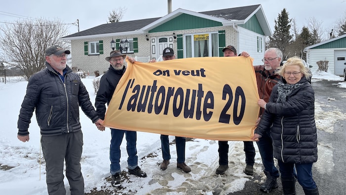 Six membres de l'Association des citoyens pour le prolongement de l'autoroute 20 tiennent une grande banderole qui porte la mention « On veut l'autoroute 20 ». 