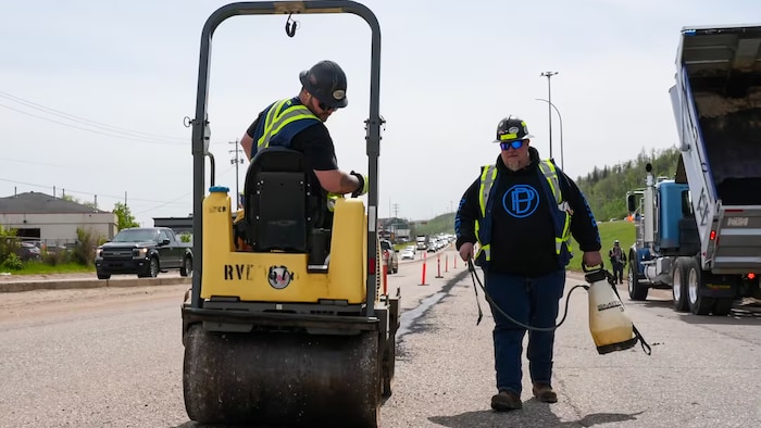 Deux bénévoles comblent des nids-de-poule avec de l'asphalte sur un tronçon de l'autoroute 63.