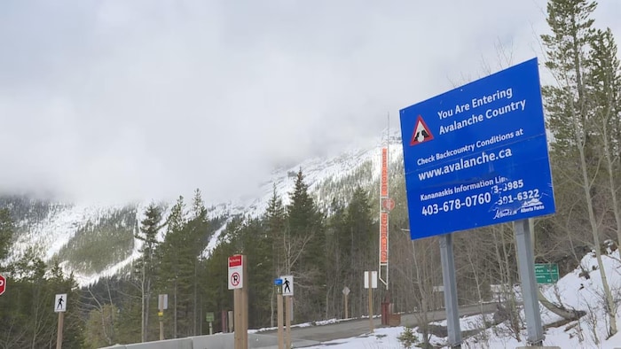 Un panneau avertissant que la zone est sujette à des avalanches devant des montagnes enneigées.