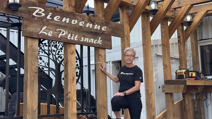 Une femme pose à côté d'une structure en bois portant une enseigne de restaurant.