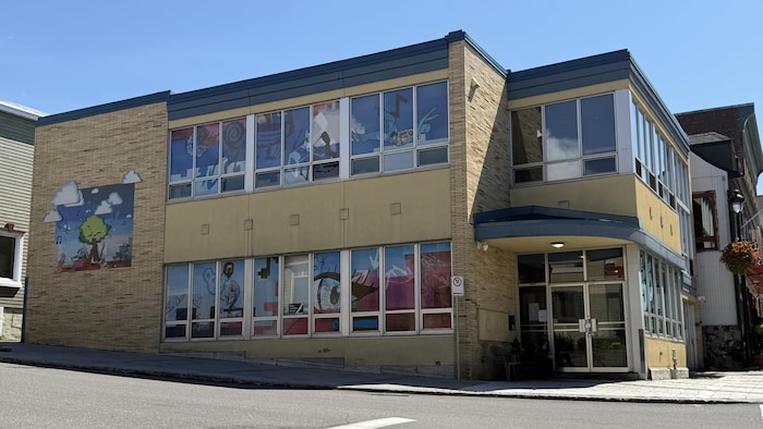 Un bâtiment moderne de deux étages avec des fresques colorées sur ses vitres et murs se dresse au coin d'une rue en pente.