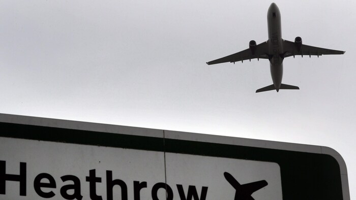 Un avion vole au-dessus d'une pancarte sur laquelle on peut lire le nom de l'aéroport.