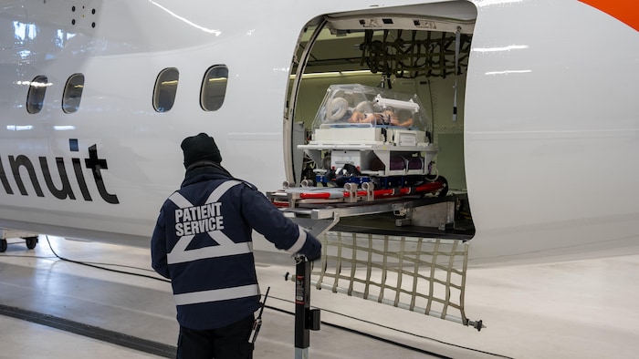 Un homme fait monter une civière avec un incubateur dans l'avion.