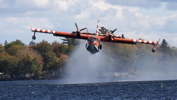Un petit avion rouge et blanc vole à moins de deux mètres au-dessus du lac où il va puiser de l'eau.