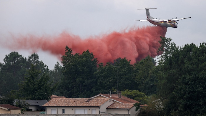 Un avion à hélices largue un produit semblable à une épaisse fumée près d'une habitation au toit de tuiles.