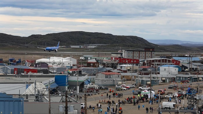 A plane lands on a strip between a small town and hills.