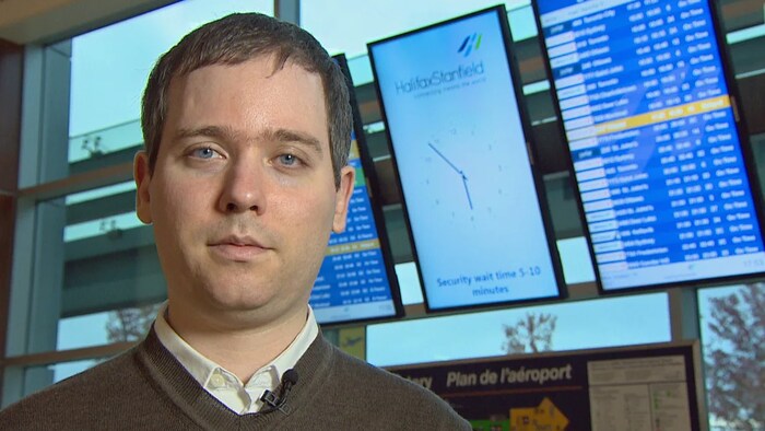 Gabor Lukacs se tient debout devant un panneau d'affichage de vols d'avions dans un aéroport. 